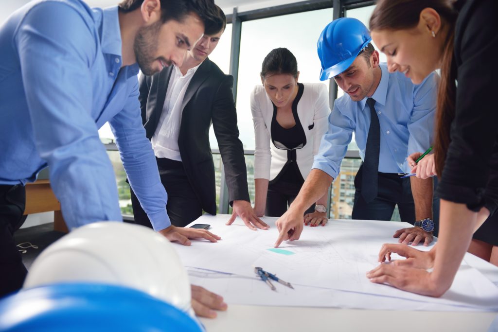 business people group on meeting and presentation in bright modern office with construction engineer architect and worker looking building model and blueprint plan print plans